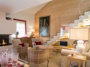Ein modernes Wohnzimmer mit Kamin, bequemen Sitzgelegenheiten, einem Flachbildfernseher und einer Treppe.