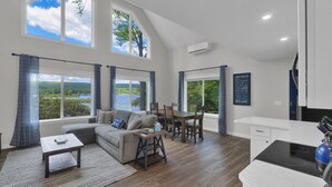 Un grand espace de vie avec vue sur un lac, comprenant une table à manger, un canapé et un coin cuisine.