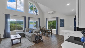 Amplia sala de estar con vistas a un lago, una mesa de comedor, un sofá y una zona de cocina.