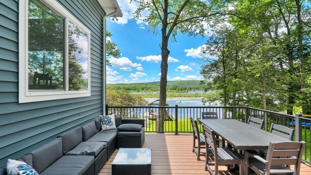 Une terrasse avec un canapé, une table et des chaises, donnant sur un lac et une végétation luxuriante.