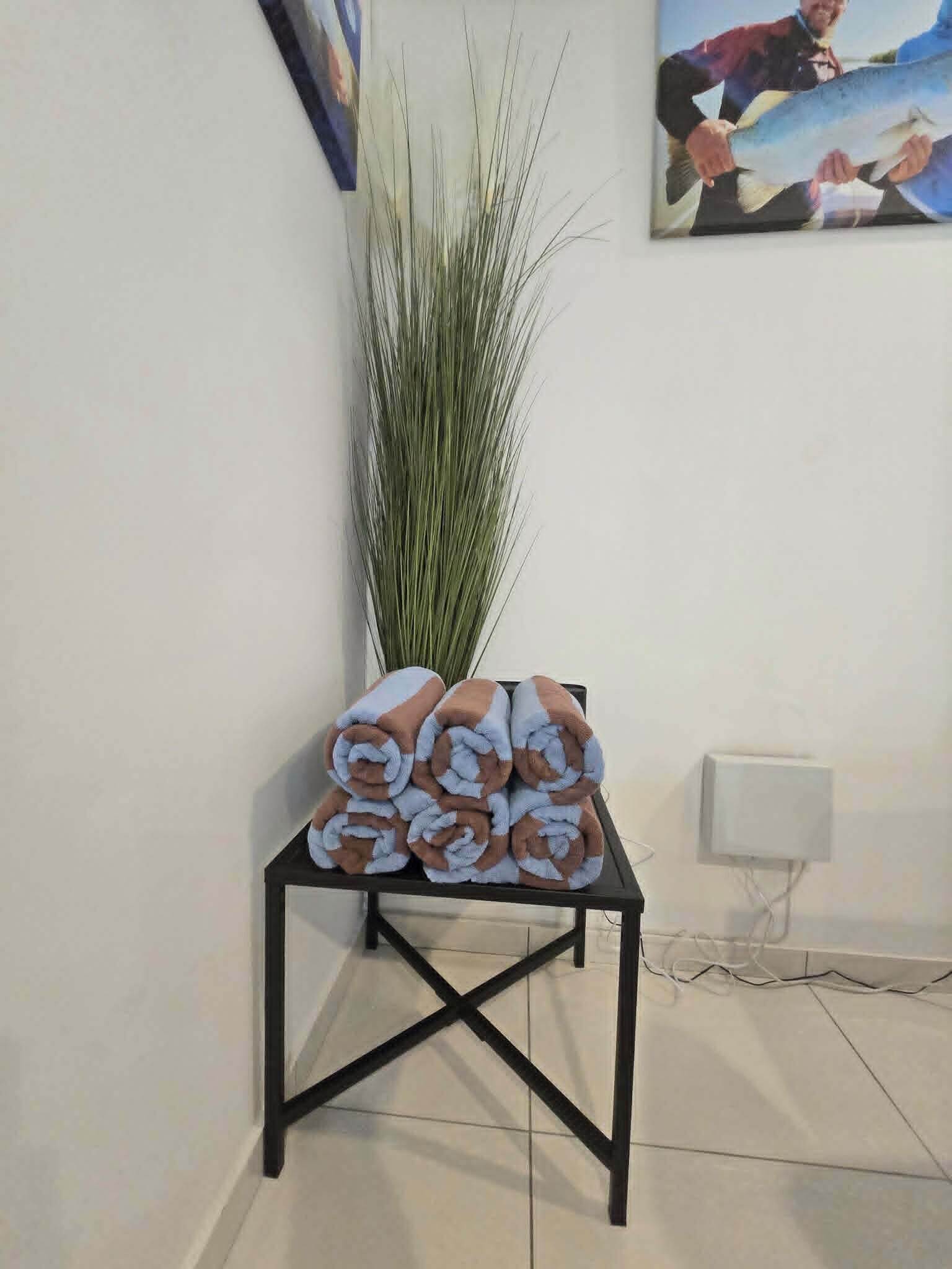 Une petite table noire avec des serviettes enroulées et une grande plante verte.