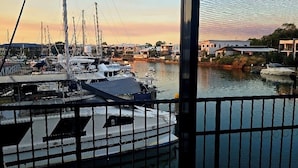 Un puerto deportivo con barcos amarrados, cielo despejado y vista de edificios a lo lejos.