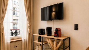 Ein modernes Zimmer mit an der Wand befestigtem Fernseher, einem Holzkonsolentisch mit Kaffeemaschine, Toaster und einer Vase mit Trockenpflanzen.