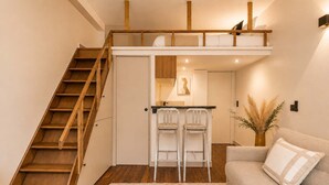 Ein Schlafzimmer im Loft-Stil mit einer Holztreppe, einer Küchenzeile, einem Sofa und einem Couchtisch.