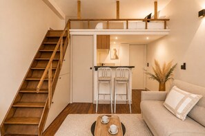 A loft-style bedroom with a wooden staircase, a kitchenette, a sofa, and a coffee table. - Renovated studio with mezzanine in Le Marais (Paris)