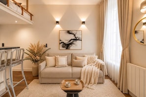 A living room with a sofa, coffee table, and a painting on the wall. - Renovated studio with mezzanine in Le Marais (Paris)