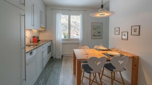 Une cuisine moderne avec des meubles blancs, une table à manger en bois et une fenêtre agrémentée de rideaux.