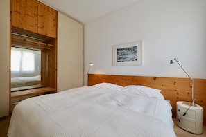 Ein Schlafzimmer mit Bett, Holzschrank, Nachttischlampe und einem gerahmten Bild an der Wand.