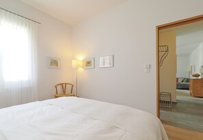 Ein Schlafzimmer mit einem Bett, einem Sessel, einer Lampe und gerahmten Bildern an der Wand.