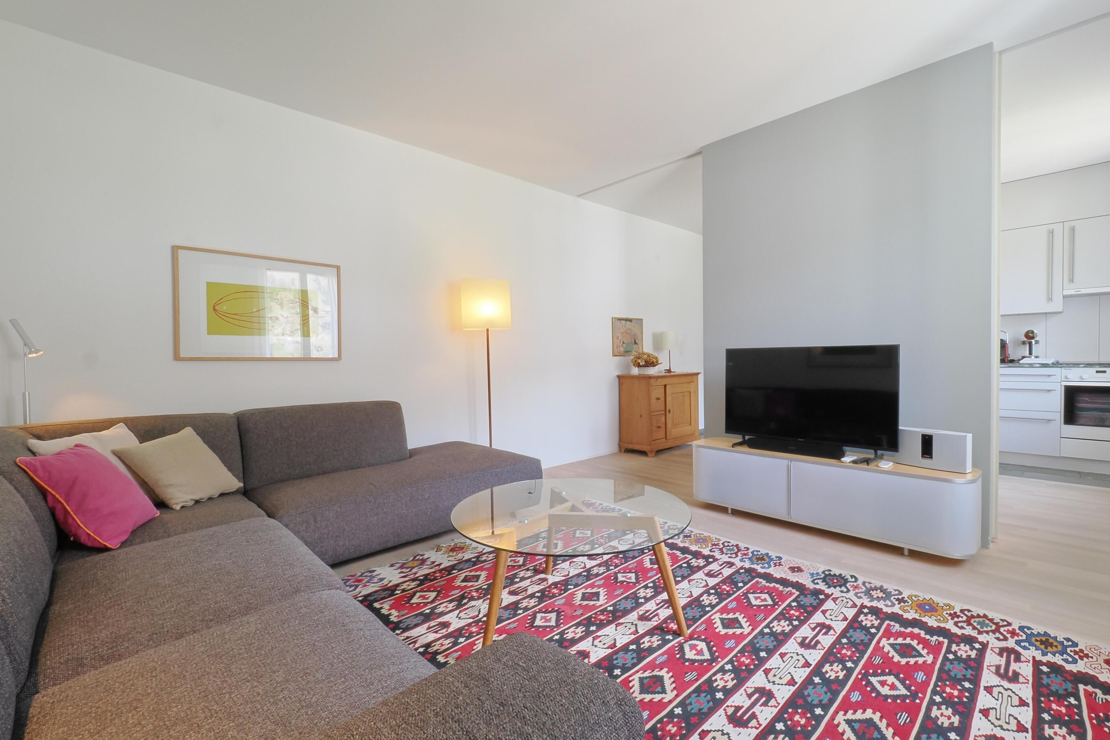 Een moderne woonkamer met een bank, een glazen salontafel en een flatscreen televisie.