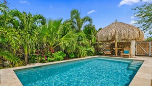 Piscina com estrutura de palha, rodeada por plantas tropicais exuberantes.