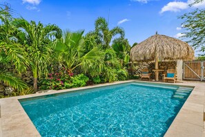 A swimming pool with a thatched-roof structure, surrounded by lush tropical plants. - Picaron 19G - B (Santa Cruz)