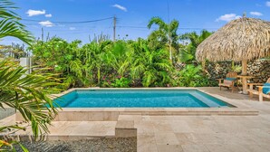Piscina rodeada por plantas tropicais e uma construção com telhado de palha.
