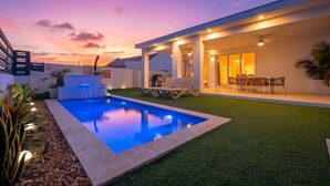 A modern house with a swimming pool, outdoor seating, and a well-lit patio area. - Caya Erasmus 18 (Oranjestad)