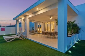 Een modern terras buiten met loungezetels, een eettafel en plafondventilatoren.