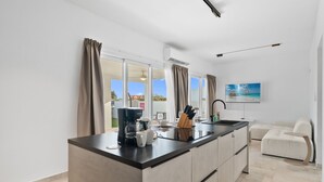 A modern kitchen with a central island, a dining area with a sofa, and a TV mounted on the wall. - Caya Erasmus 18 (Oranjestad)