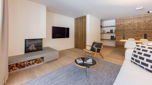 Un salon moderne doté d’une cheminée, d’un téléviseur à écran plat, d’un coin repas avec un mur en bois et d’un canapé.