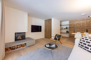 Ein modernes Wohnzimmer mit Kamin, Flachbildfernseher, Essbereich mit Holzwand und einer Couch.
