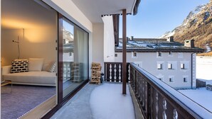 Un balcon avec un canapé, une porte vitrée, une pile de bois de chauffage et une vue sur une montagne.