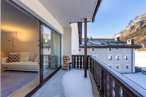 Ein Balkon mit einer Couch, einer Glastür, einem Holzstapel und Blick auf einen Berg.