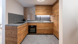 Une cuisine compacte dotée de meubles en bois, d’un plan de travail en granit, d’un four encastré et d’un luminaire moderne.