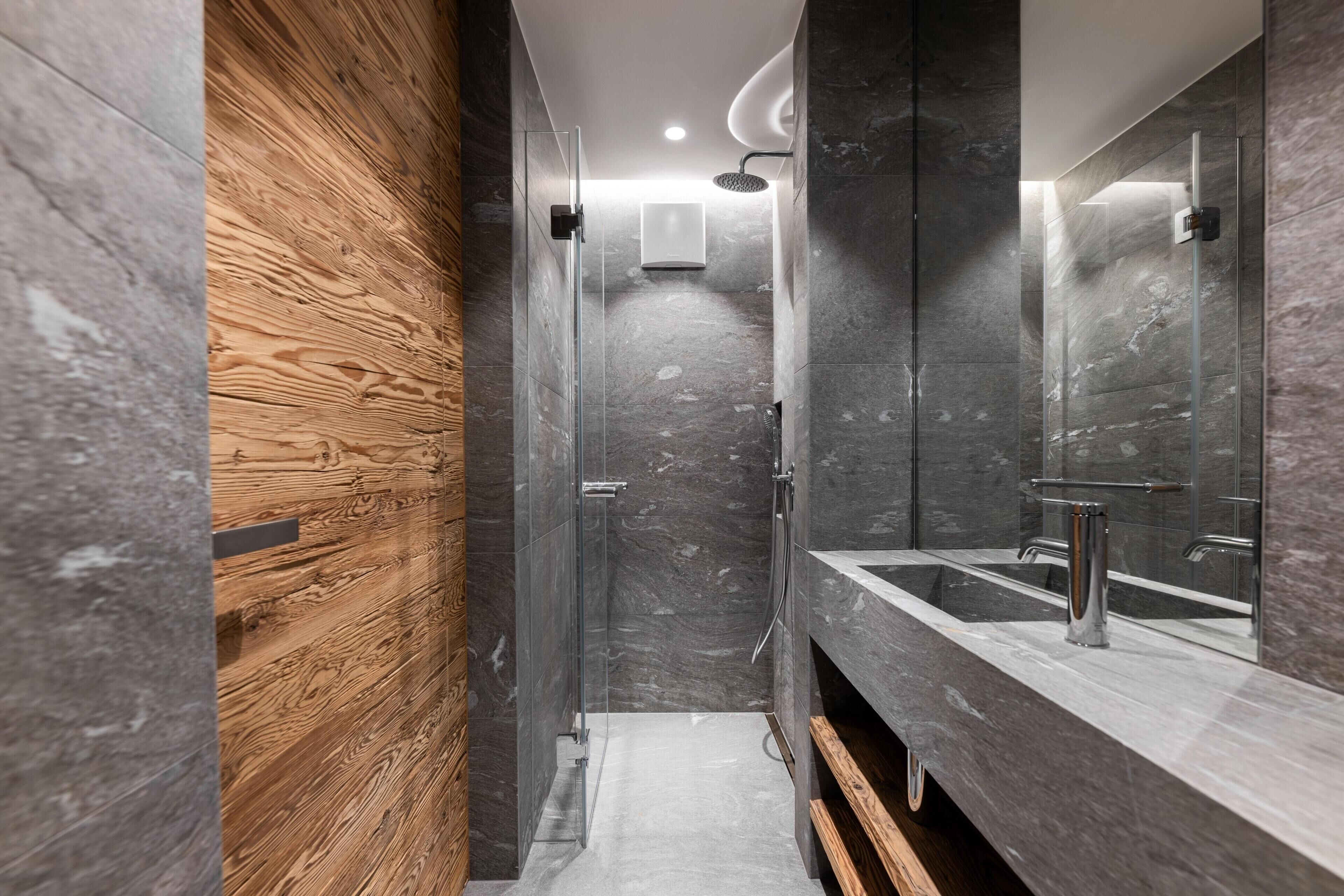 A modern bathroom with a wooden wall, a glass shower enclosure, and a marble sink.