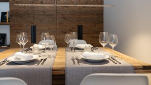 Une table à manger dressée avec des assiettes, des couverts et des verres à vin, sur fond d’un mur en bois et d’un luminaire suspendu.