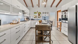 Uma cozinha moderna com armários brancos, uma mesa de jantar de madeira e uma geladeira de aço inoxidável.