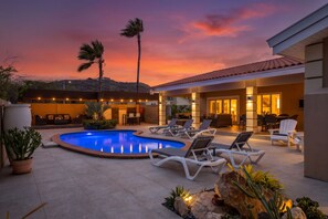 A pool area with lounge chairs, a palm tree, and a building with a tiled roof.
