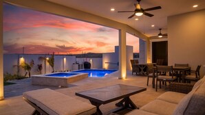 Un área de descanso al aire libre moderna con piscina, mobiliario y vistas al atardecer.