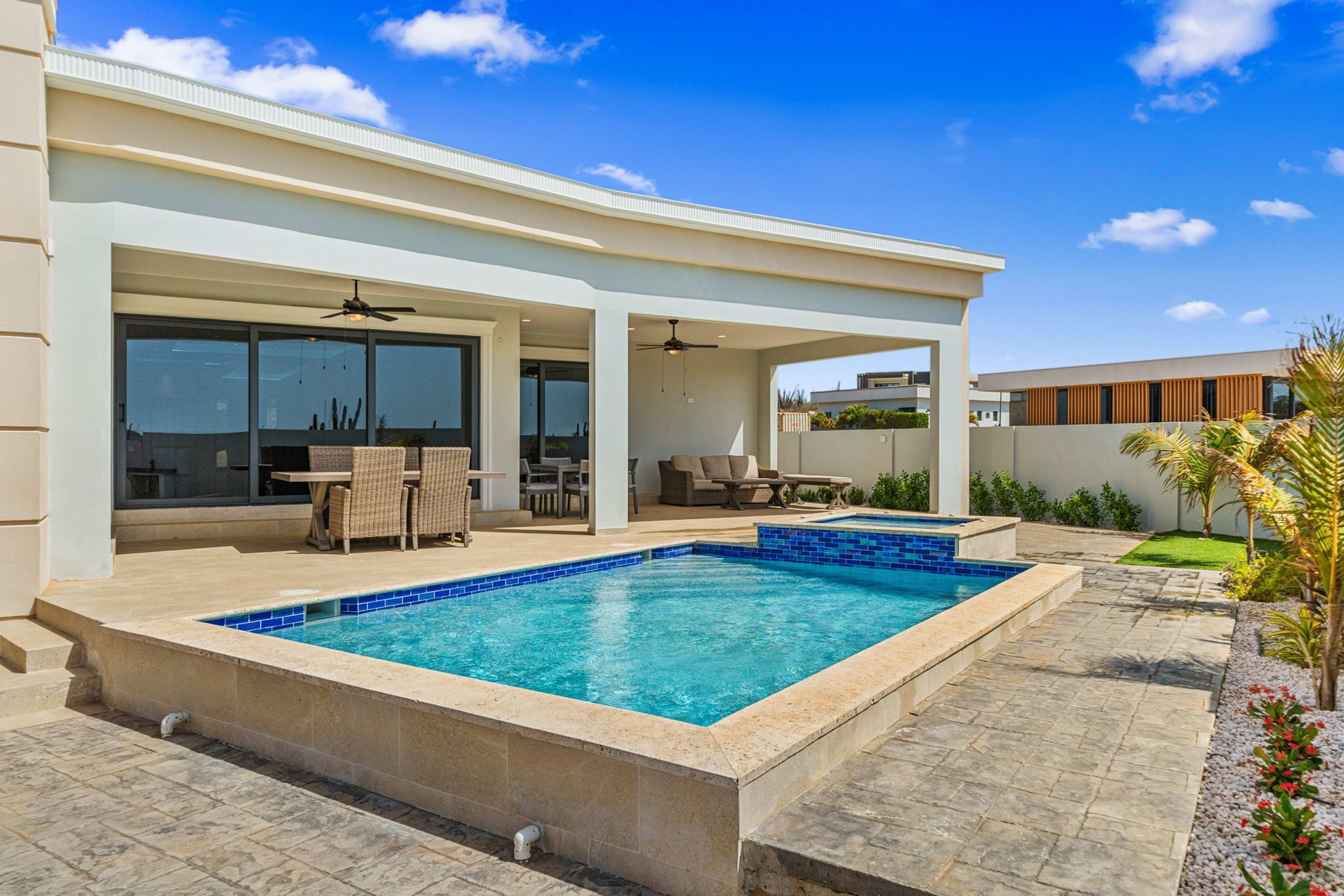 Una casa moderna con piscina, mobiliario de exterior y un porche cubierto.