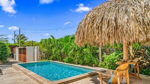 A swimming pool with a thatched roof, surrounded by lush greenery and a stone wall. - Picaron 19G - C (Santa Cruz)