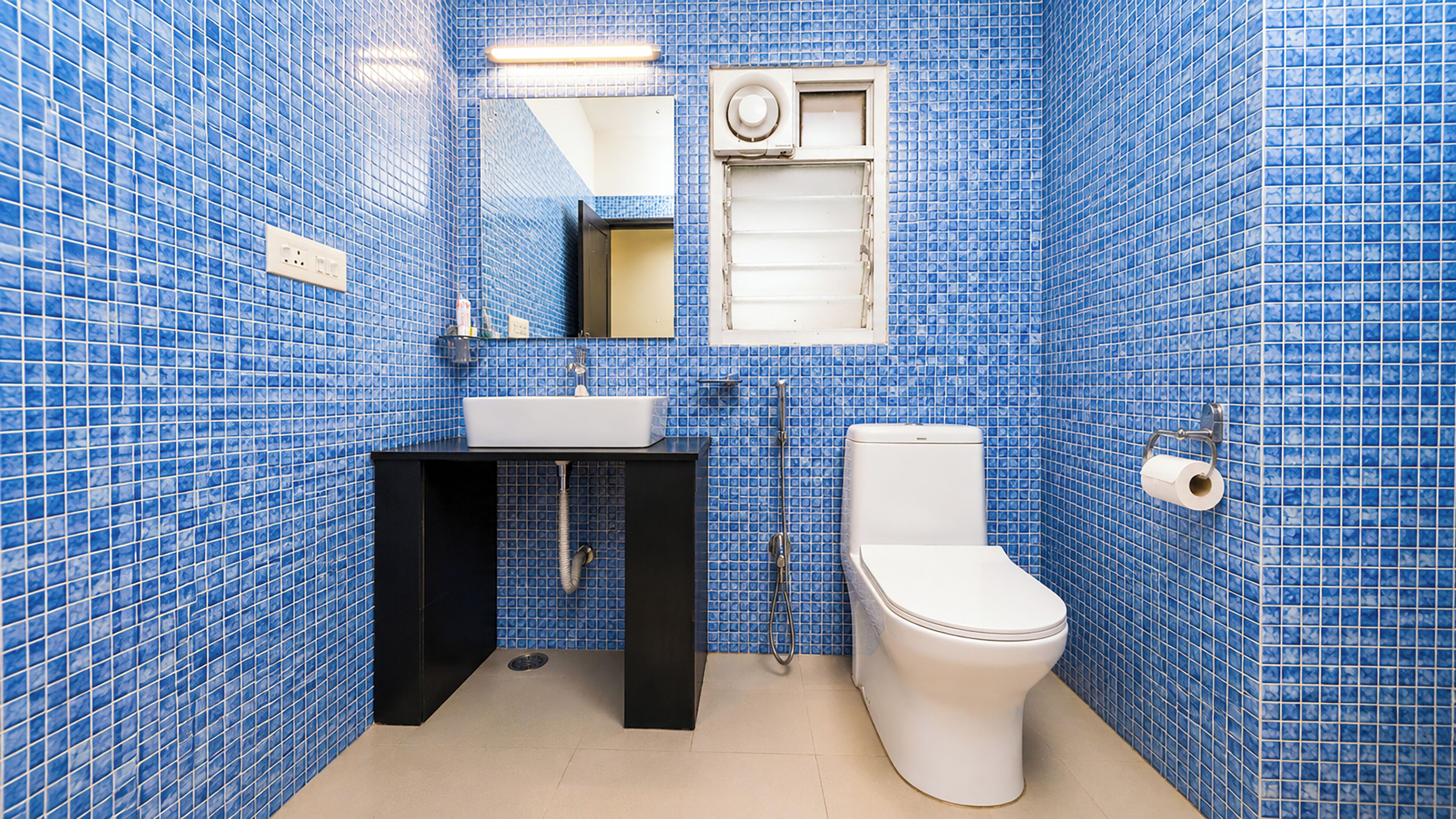 A bathroom with blue tiled walls, a white sink, a black cabinet, a toilet, and a shower.