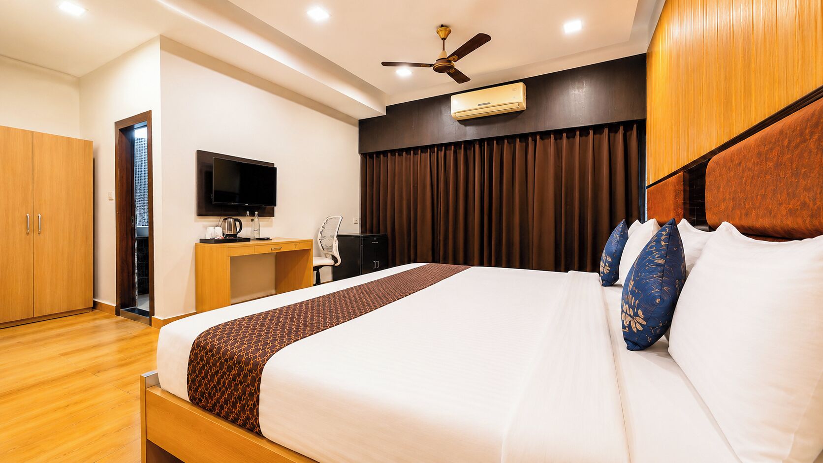 A hotel room with a bed, a desk, a television, and a wardrobe.