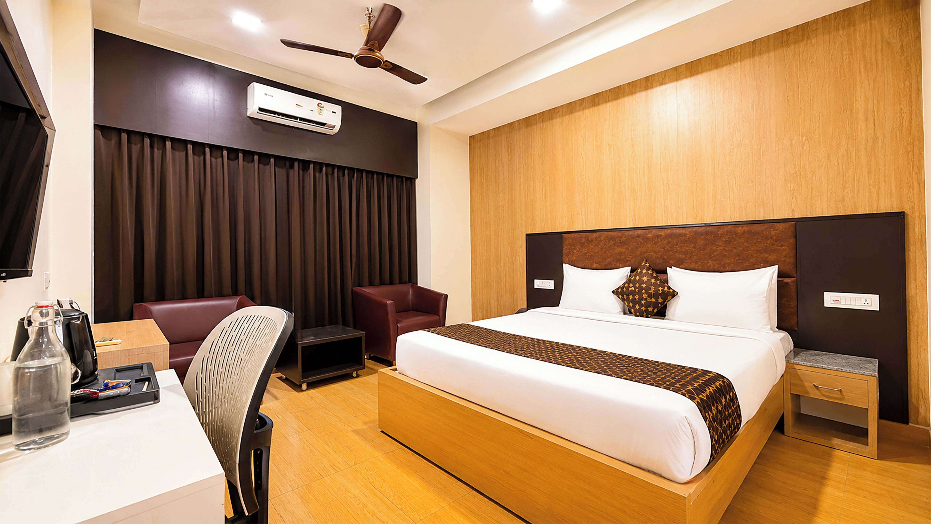 Una habitación de hotel con cama, escritorio, silla, televisor y aire acondicionado.