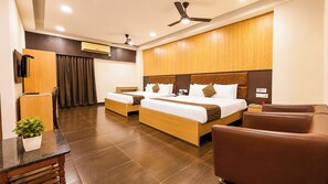 A hotel room with two beds, a desk, a chair, a plant, and a ceiling fan.
