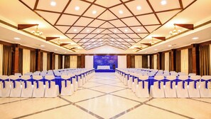 Un salón de conferencias con filas de sillas, un escenario y un cartel.