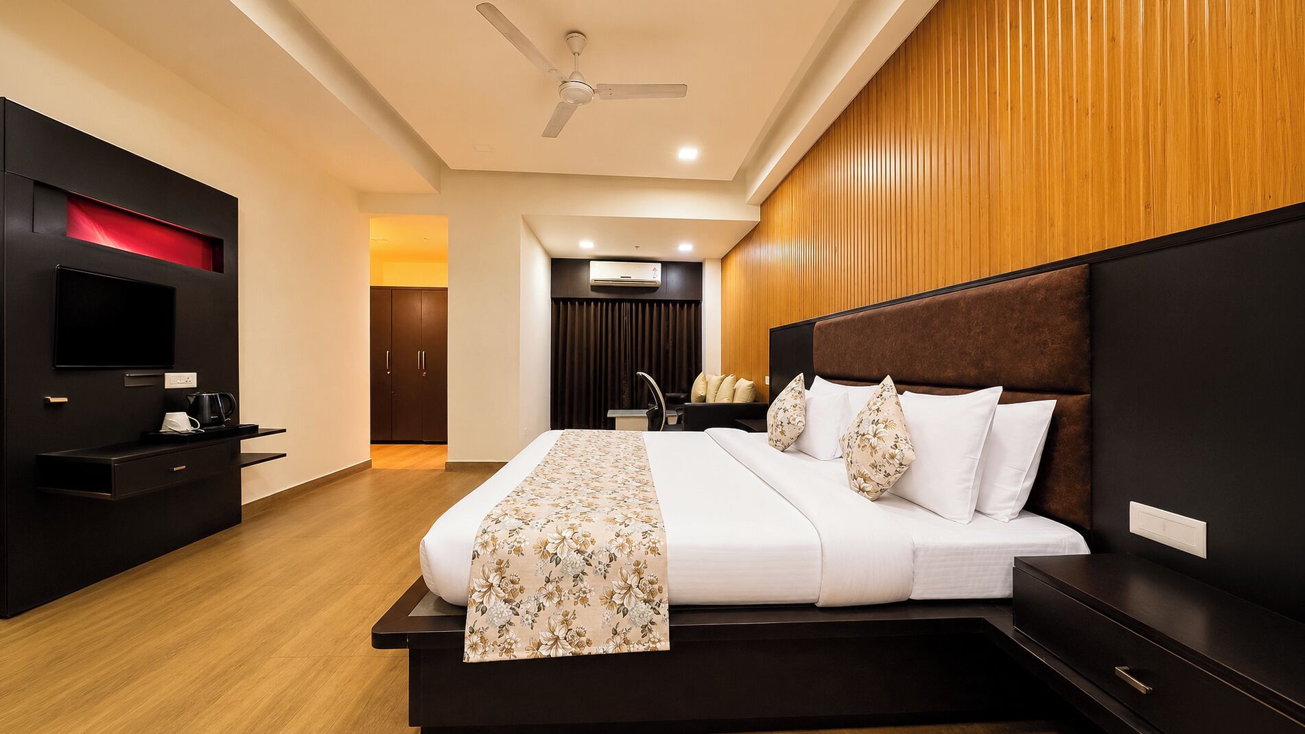 A modern hotel room with a large bed, a flat-screen TV, a desk, and a ceiling fan.