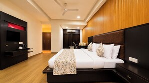 A modern hotel room with a large bed, a flat-screen TV, a desk, and a ceiling fan. - Sumitel Central Park Hotel & Banquet (Jalpaiguri)