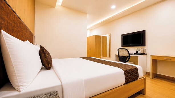 Una habitación de hotel con cama, escritorio, silla, televisor y espejo.