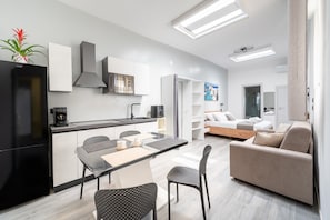 A modern kitchen with a dining area, a sofa, and a bed in a well-lit living space.