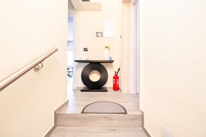 A staircase leading to a room with a modern design, including a black circular wall decoration, a white vase with flowers, and a red fire extinguisher.