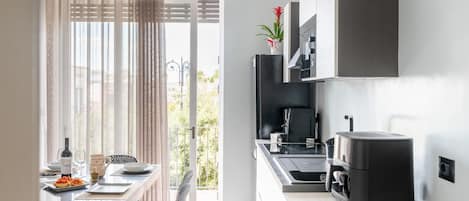 Una cocina moderna con cafetera integrada, un comedor con mesa dispuesta para dos personas y vistas al exterior.