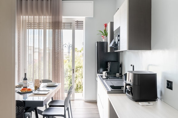 A modern kitchen with a built-in coffee machine, a dining area with a table set for two, and a view of the outdoors.
