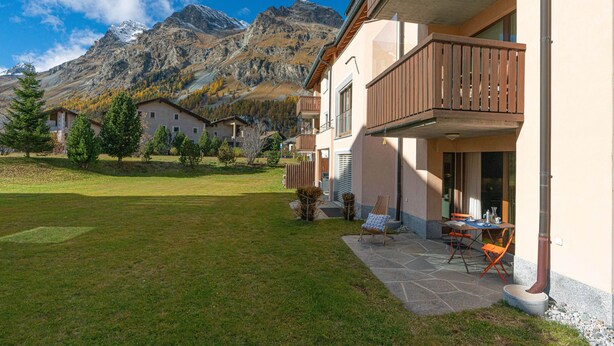 Ein Wohngebäude mit Balkon, einer Terrasse mit Gartenmöbeln und einer Bergkulisse im Hintergrund.