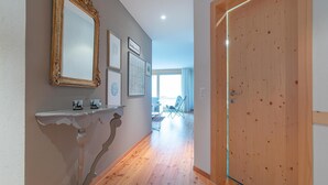 Ein Flur mit Holzboden, einer weißen Wand mit einem dekorativen Spiegel und einer Holztür.