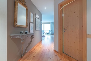 Ein Flur mit Holzboden, einer weißen Wand mit einem dekorativen Spiegel und einer Holztür.