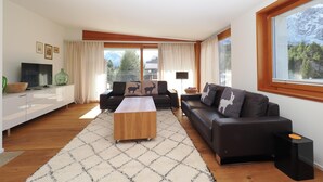 Una sala de estar moderna con un sofá, una mesa de centro, un televisor y un amplio ventanal con vistas a la montaña.