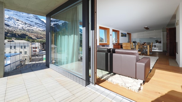 Una sala de estar moderna con un amplio ventanal corredera, un sofá y vistas a un paisaje montañoso.