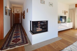 A hallway with a patterned rug, a glass display case with decorative items, and a white cabinet with a green vase. - Chesa Soldanella – Stylish Vacation Rental with Valley and Mountain Views (Bregaglia)